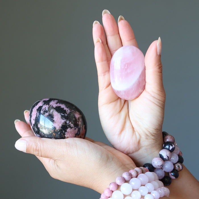 hands wearing and holding rhodonite and rose quartz crystals