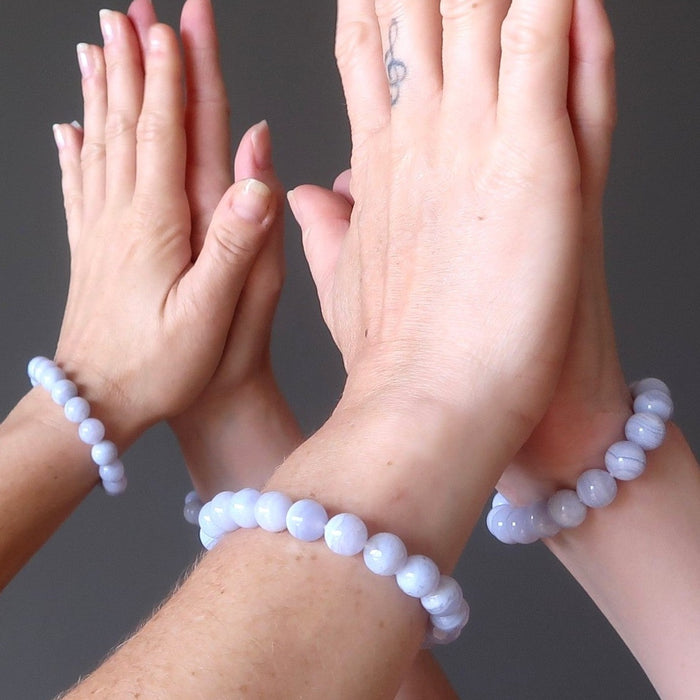 set of hands high fiving wearing blue lace agate round beaded stretch bracelets