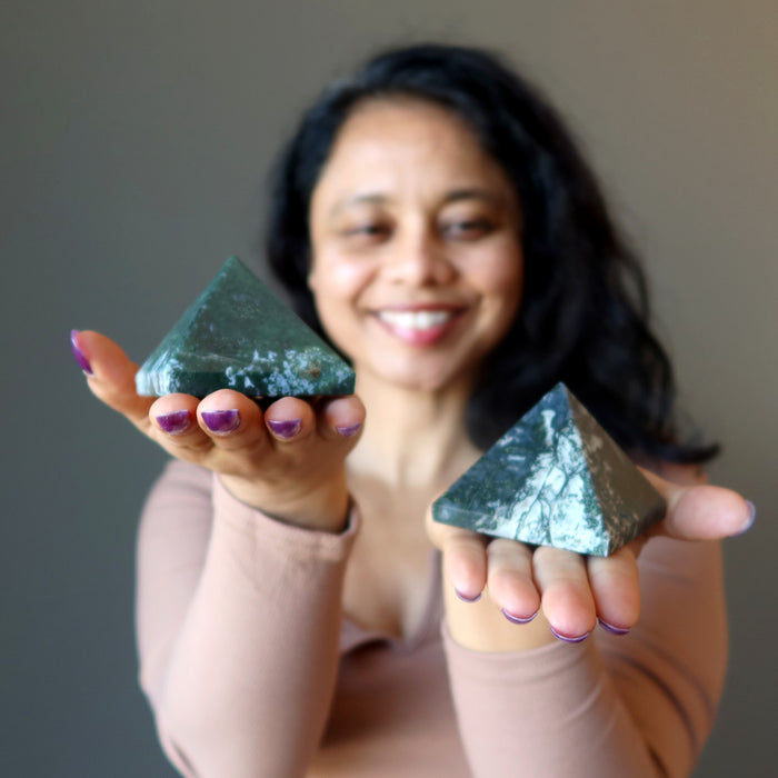 woman holding two green and white moss agate pyramids