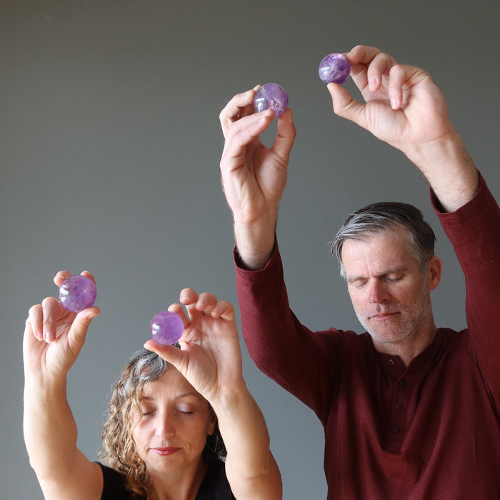 a male and a female models raising amethyst ball up 