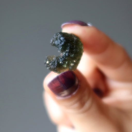 hand holding green moldavite gemstone with a scroll curl