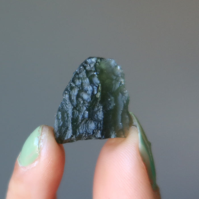 hand holding up a rough moldavite gemstone