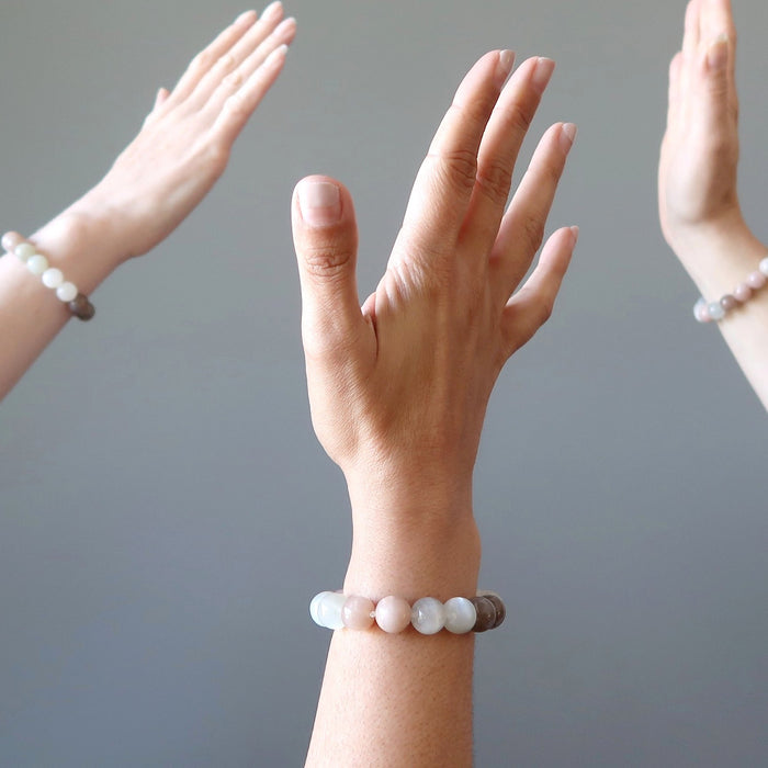 three hands wearing multi-color moonstone beaded bracelets