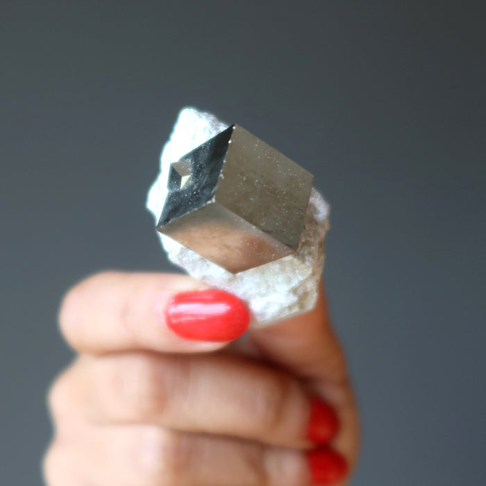 hand holding pyrite cube on white matrix