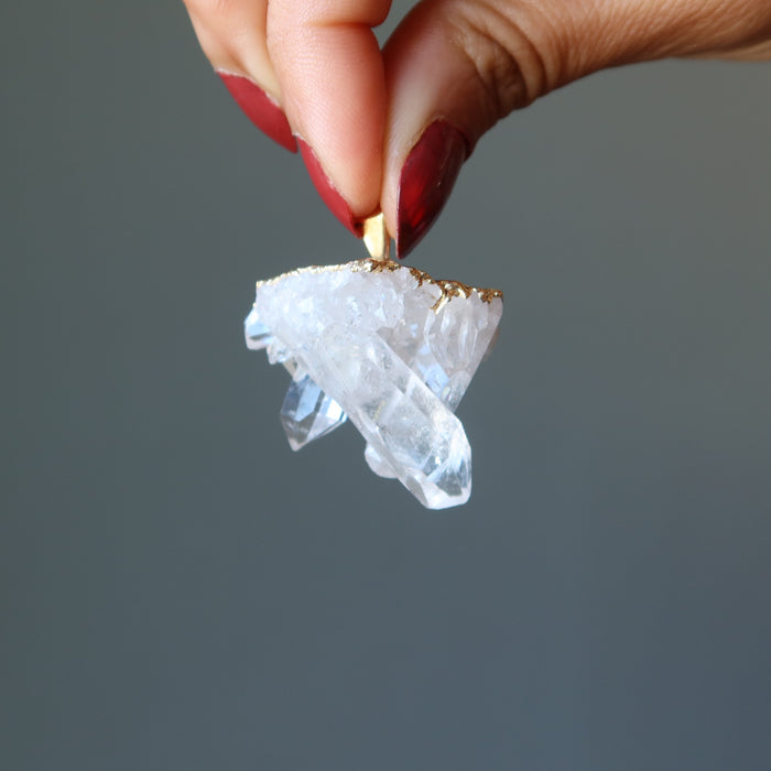hand holding raw quartz cluster pendant in gold electroplating