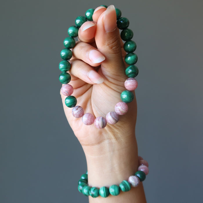 hand wearing and holding a rhodochrosite and malachite stretch bracelet