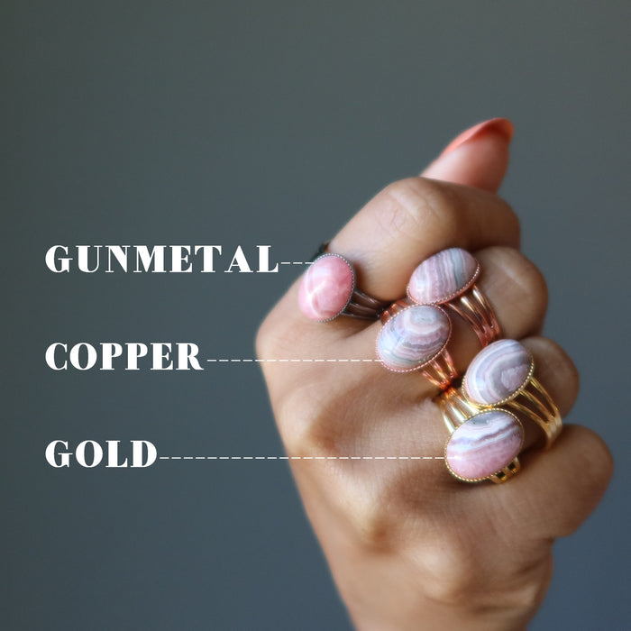 hand wearing rhodochrosite rings in gunmetal, copper and gold
