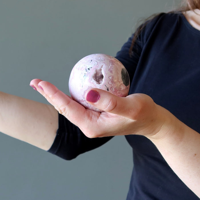 woman holding rhodonite geode sphere