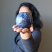 female holding forth a hand holding blue sodalite sphere