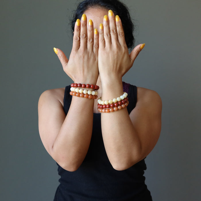 sheila of satin crystals wearing yellow calcite, orange aventurine, red jasper stretch bracelet sets on both wrists with hands covering face