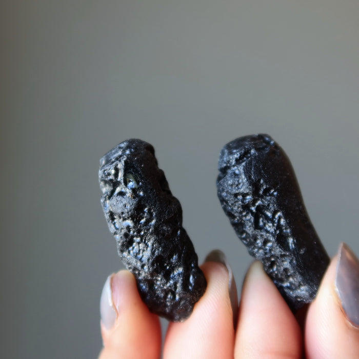 hands holding rough black tektites