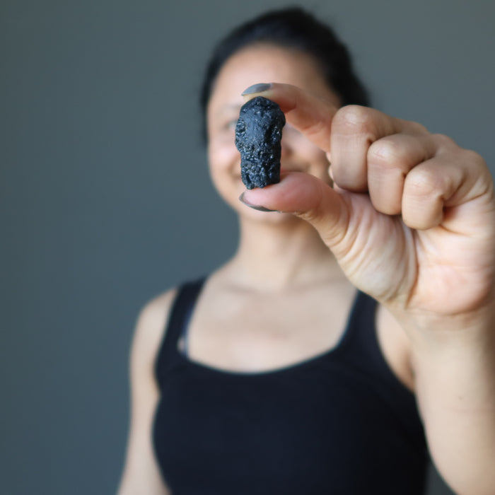 female holding a rough black tektite
