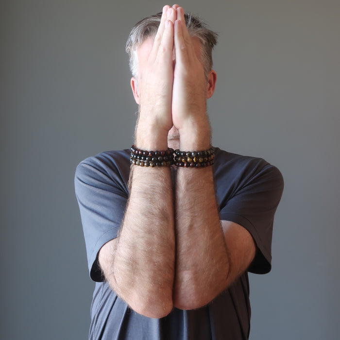 man wearing a set of three tigers eye bracelets on each wrist with hands up in prayer