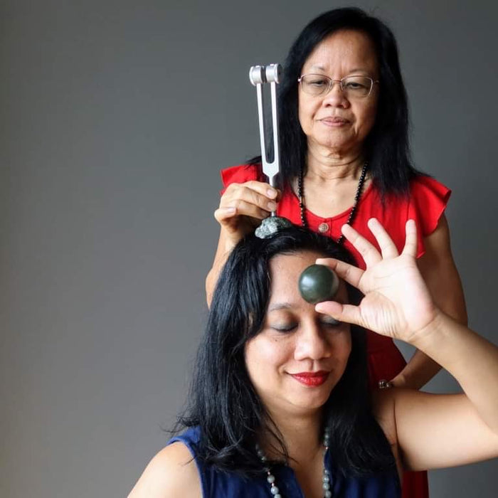 Healer using tuning fork on client with Jade on third Eye chakra