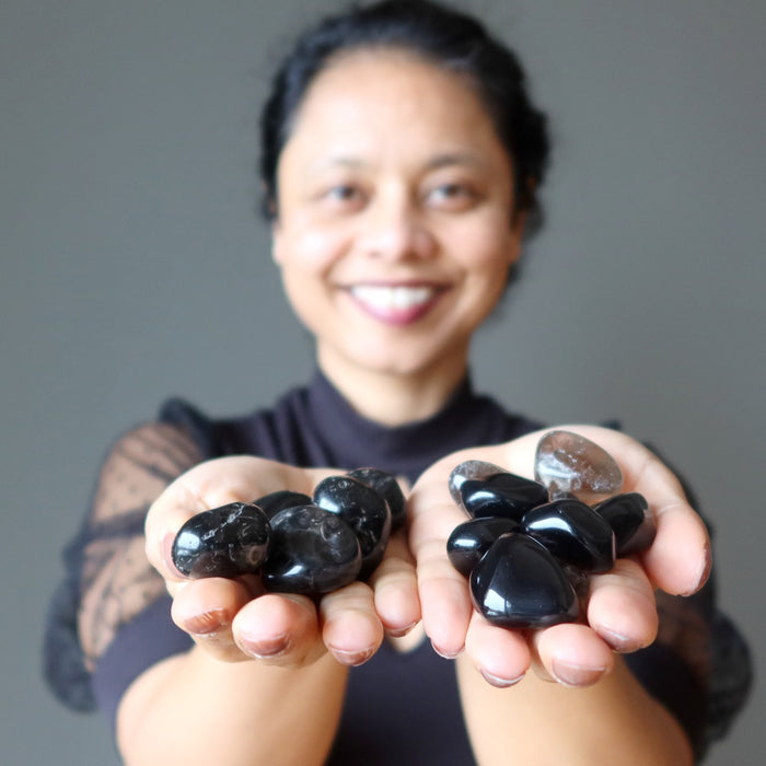 sheila of satin crystals holding black and brown protection tumbled stones