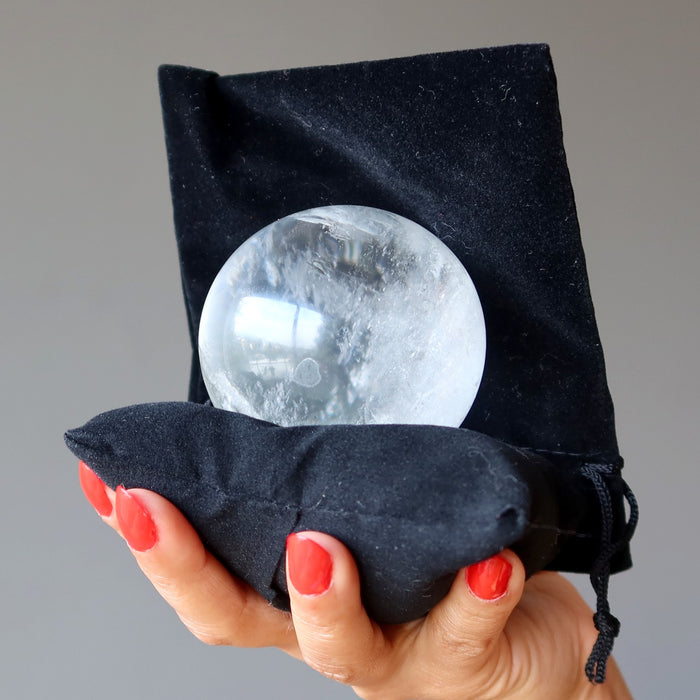 holding clear quartz sphere on black pillow