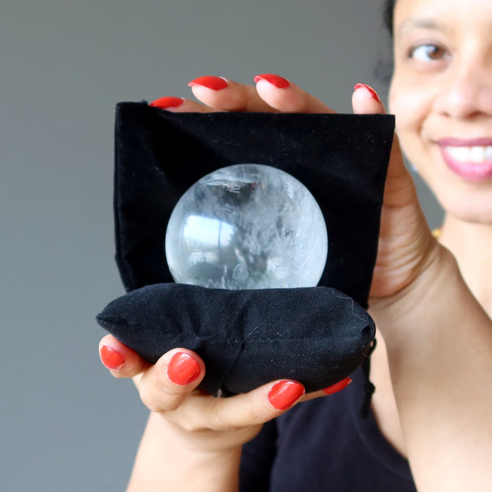 sheila of satin crystals holding a clear quartz ball on a black pillow