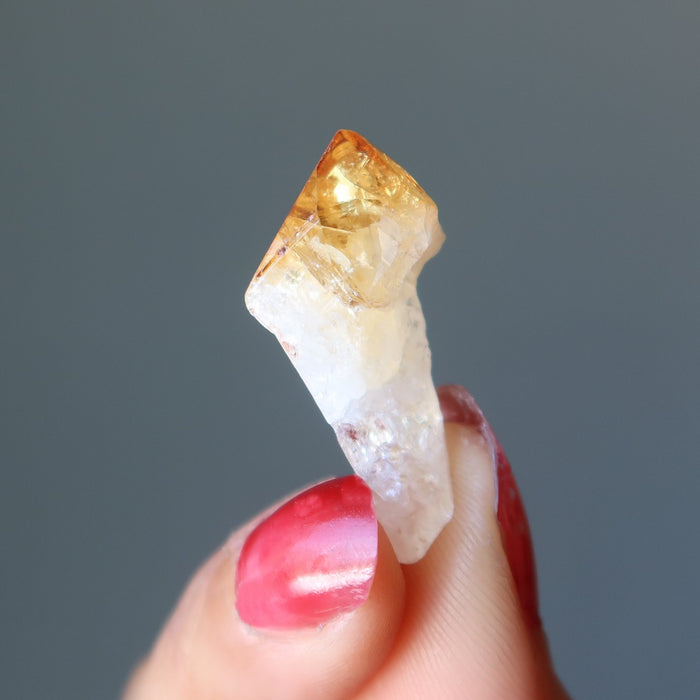 fingers holding raw yellow citrine point