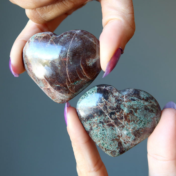 hands holding red and green garnet heart stones
