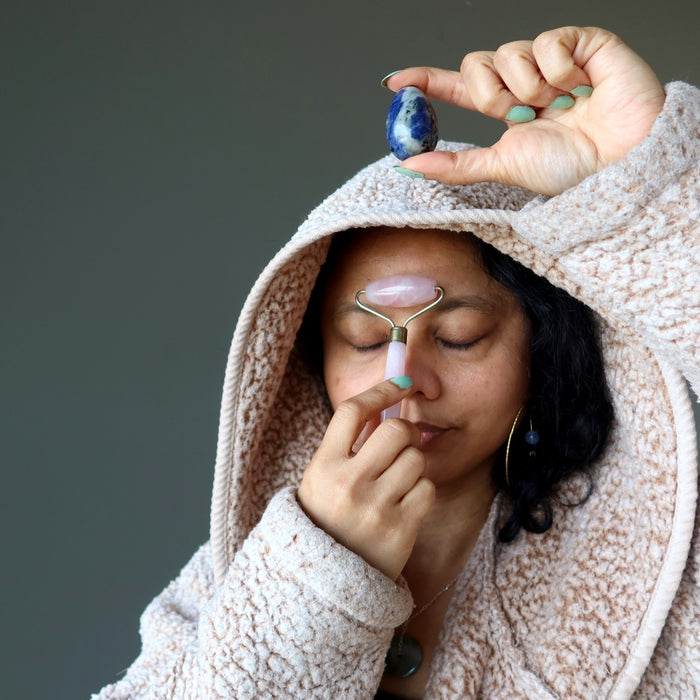 woman holding sodalite egg and using pink rose quartz roller