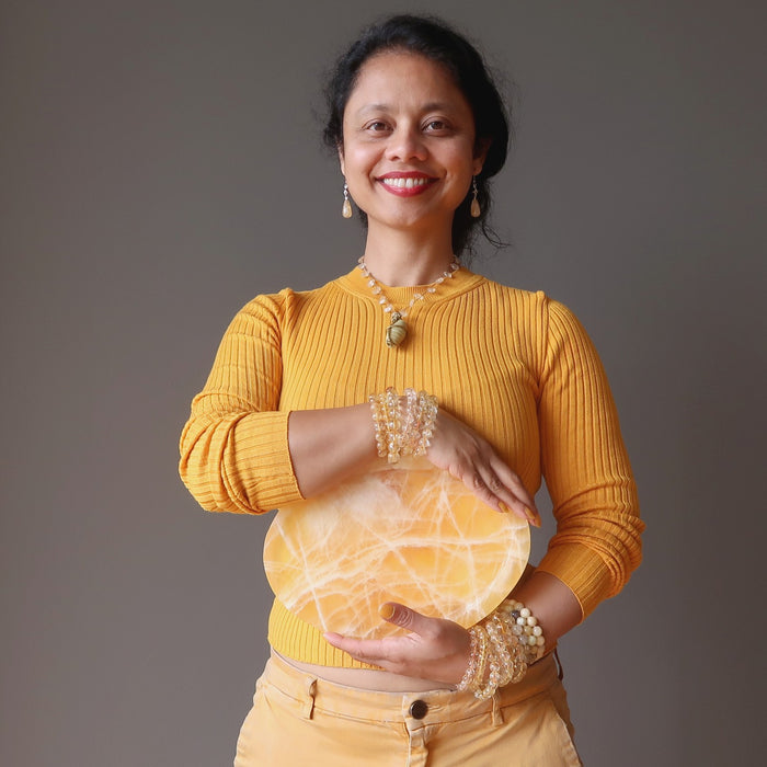 sheila of satin crystals holding a yellow calcite platter at her solar plexus chakra