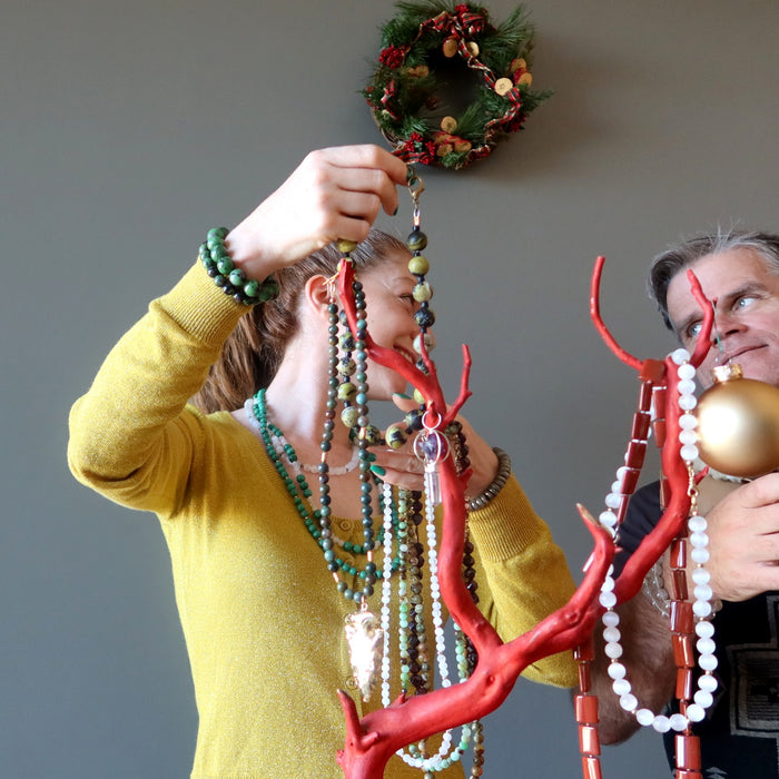 man and woman putting up crystal necklaces on a red branch in front of wreath