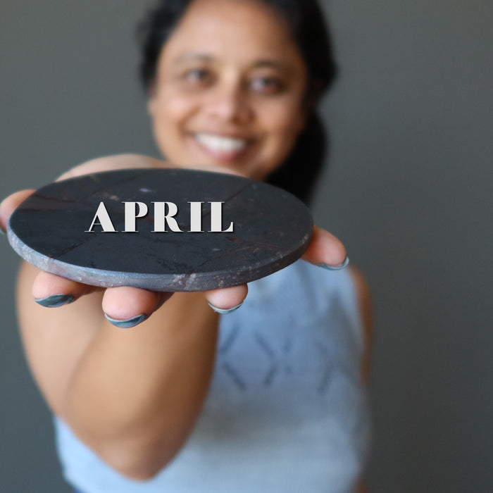 woman holding hematite circle with word APRIL