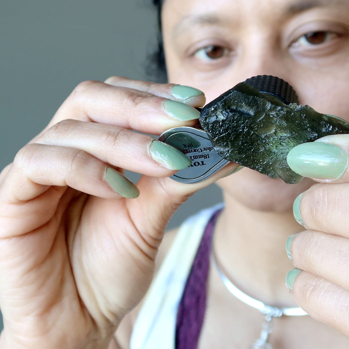 sheila of satin crystals peering into a moldavite with loupe