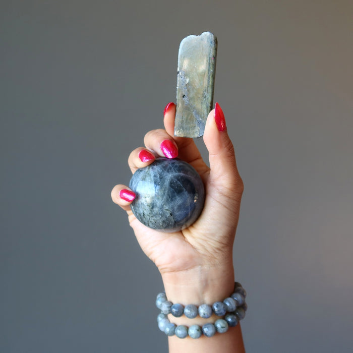 hand wearing labradorite bracelets holding a labradorite sphere and polished stone