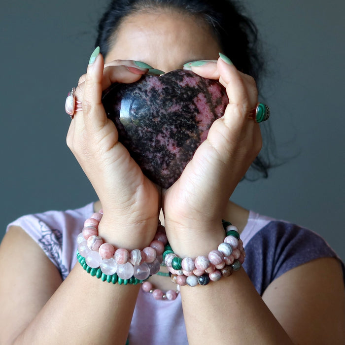 woman holding rhodonite heart wearing malachite and rhodochrosite and rose quartz jewelry