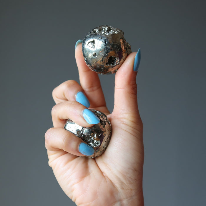 hand holding two pyrite spheres