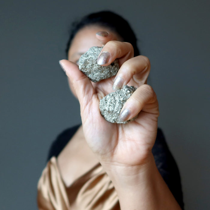 female holding two raw pyrite stones in her hand