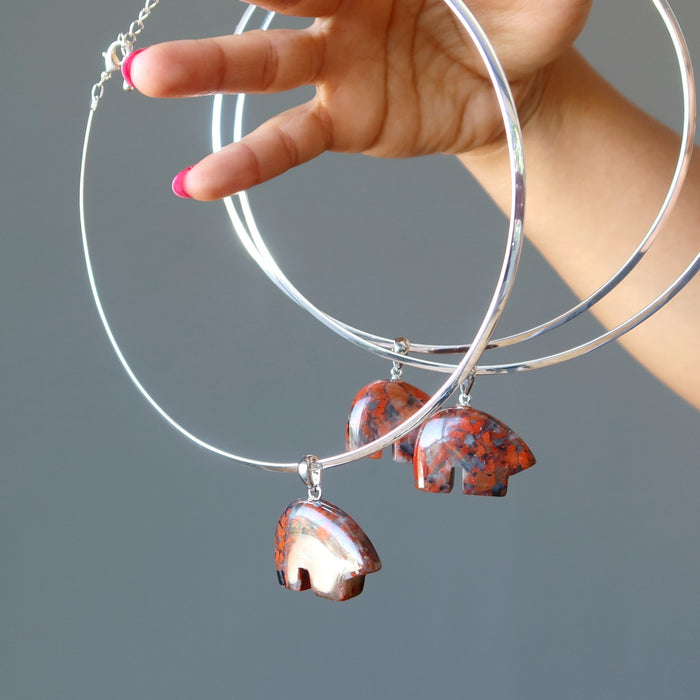 hand holding three silver chokers hanging with red jasper bear pendants