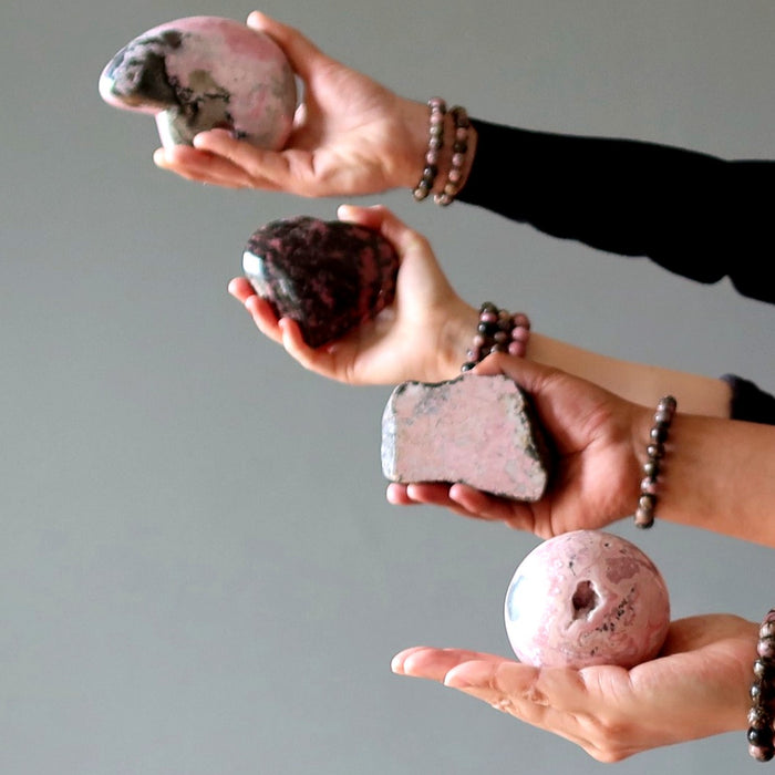 hands holding rhodonite stones