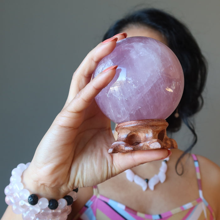 female holding a rose quartz ball in front of her face