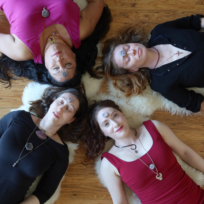 four women lying with ruby crystals in a layout