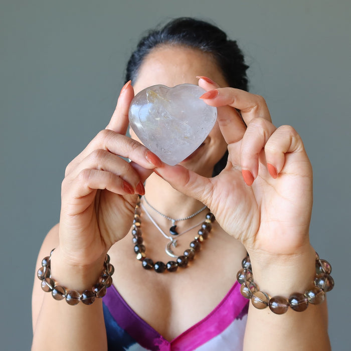 woman holding smoky quartz heart to her face wearing smoky quartz jewelry