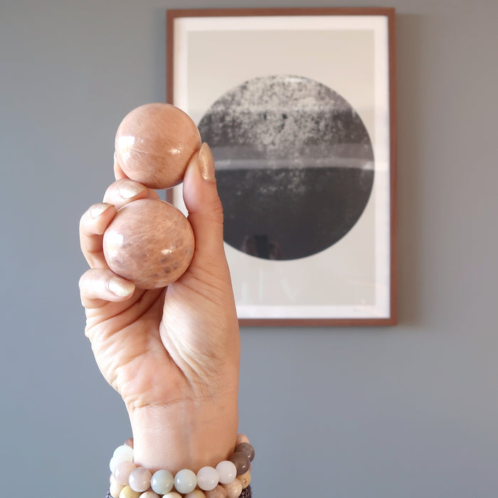 hand holding up two peach moonstone spheres in front of a moon framed picture