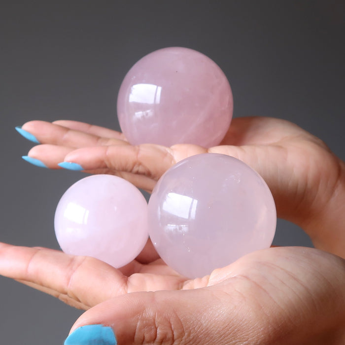 hands holding three rose quartz spheres