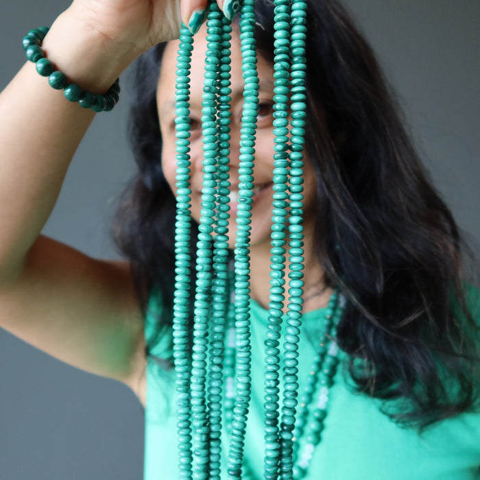 sheila of satin crystals holding strands of malachite beads in front of her