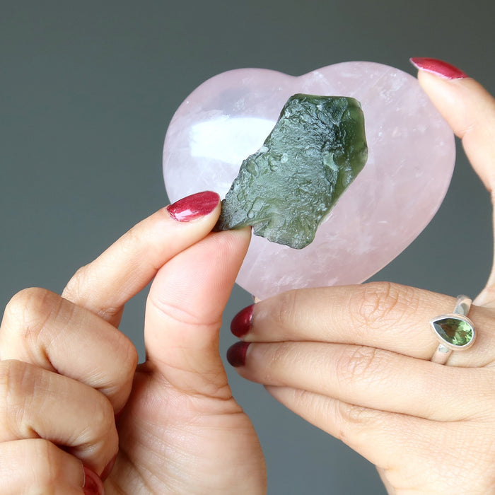 hands holding raw moldavite and rose quartz heart