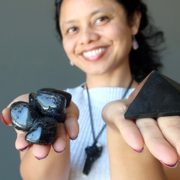 female holding black tourmaline tumbled stones and pyramid