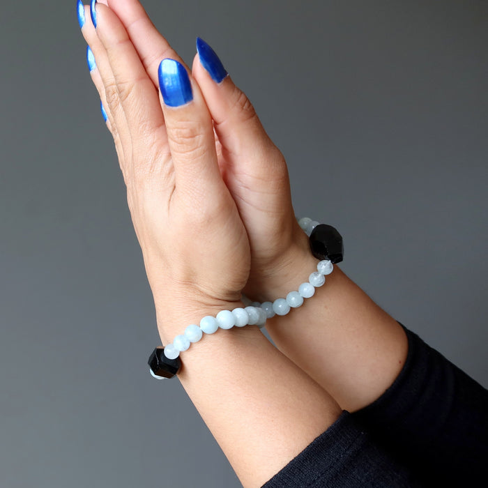 hands clasped wearing black tourmaline blue aquamarine bracelets