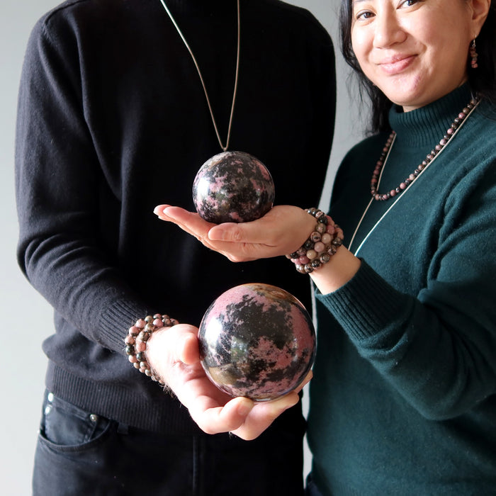 couple holding pink and black rhodonite spheres