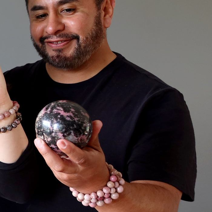 man holding pink and black rhodonite sphere