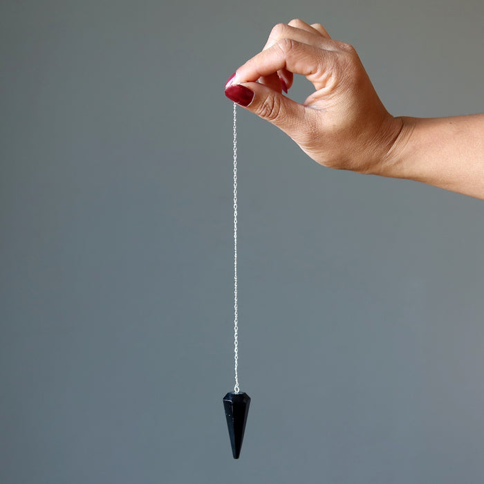 hand using black tourmaline faceted pendulum