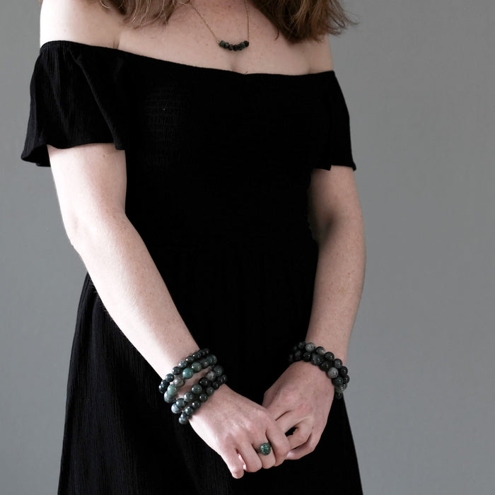 female model in black dress wearing a stack of moss agate bracelets, chrysocolla ring and ruby zoisite necklace