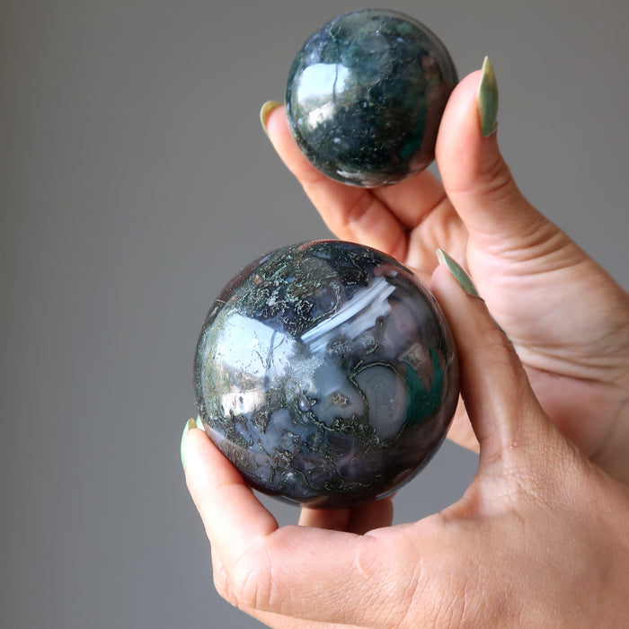 two hands holding a moss agate ball in each