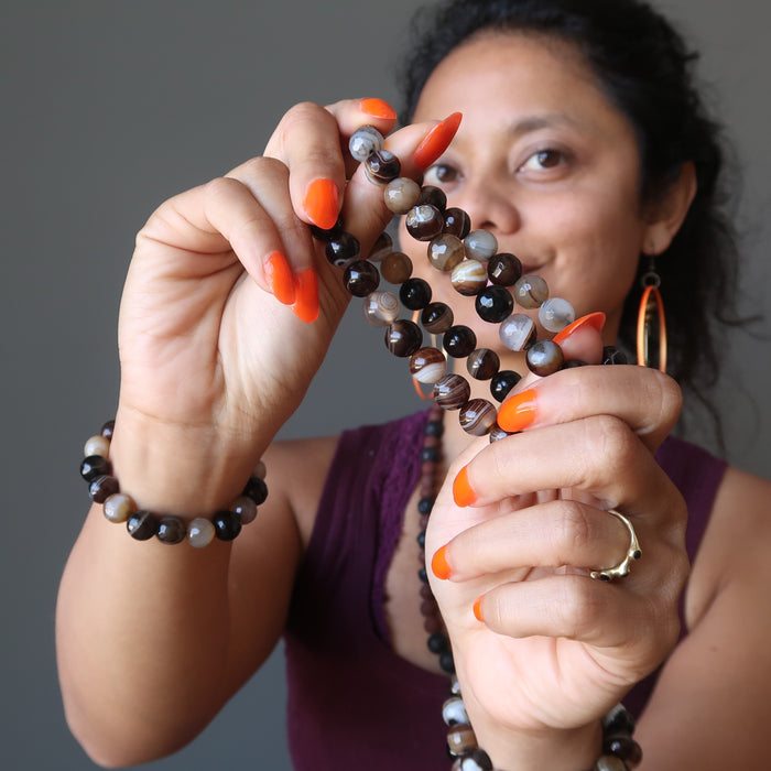 sheila of satin crystals wearing and holding banded coffee brown and black agate faceted round beaded stretch bracelets