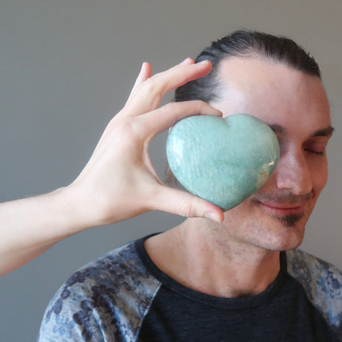 a female model hand holding light green Amazonite Heart Shiny Stone in front of a male model
